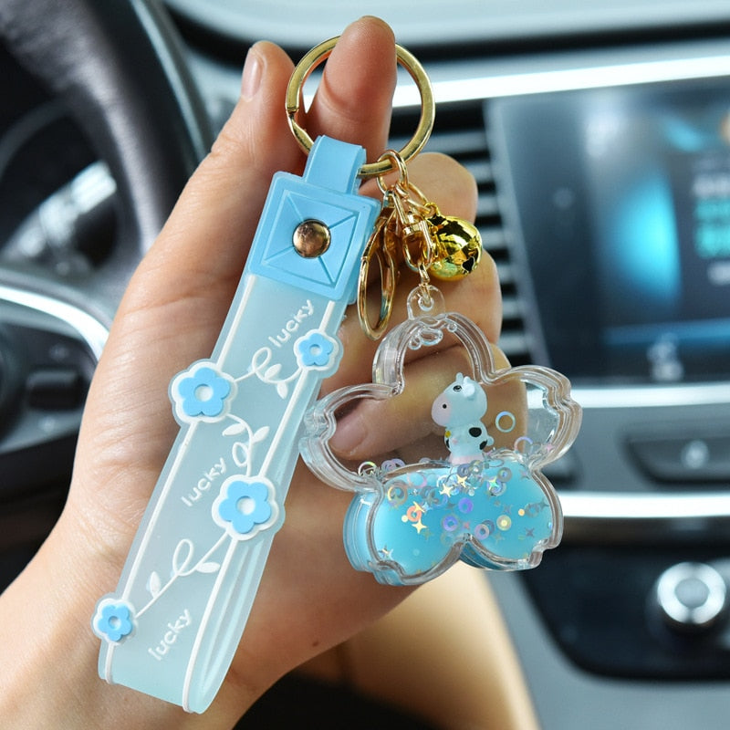 Cute blue sakura cow quicksand keychain with glitter, gold bell, and "lucky" floral ribbon. Resin and zinc alloy.