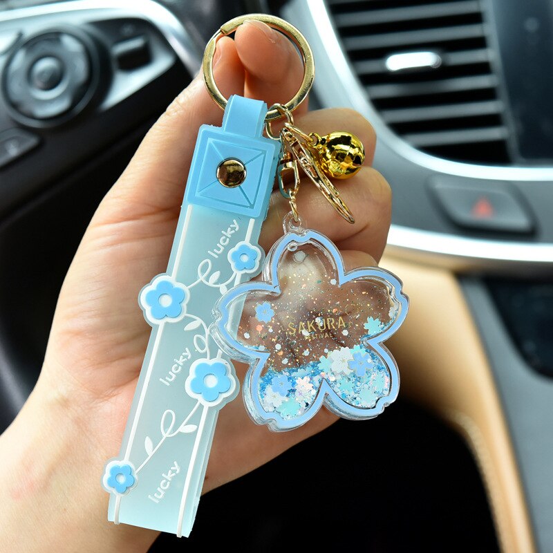 Blue Sakura Cow quicksand keychain with glitter, flower charm, gold bell, and lucky ribbon.