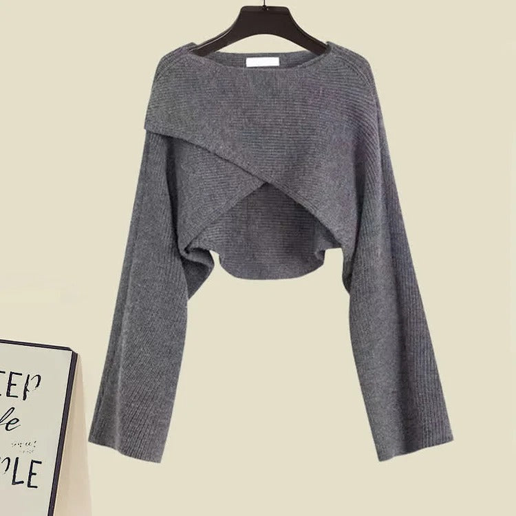 Grey knit cropped sweater with crossover design and long sleeves, paired with a knee-length asymmetrical slip dress.