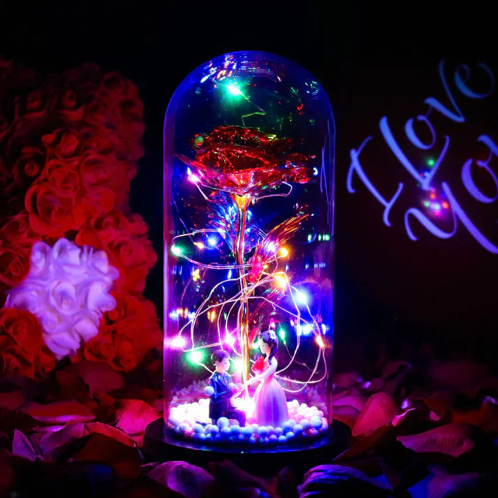 LED iridescent rose in glass dome with warm white lights, wooden base, and couple figurines; perfect gift.