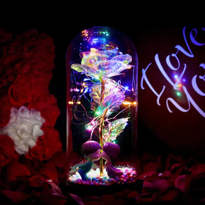 Iridescent LED rose in glass dome with warm white lights, wooden base, and kissing figurines. Perfect gift.