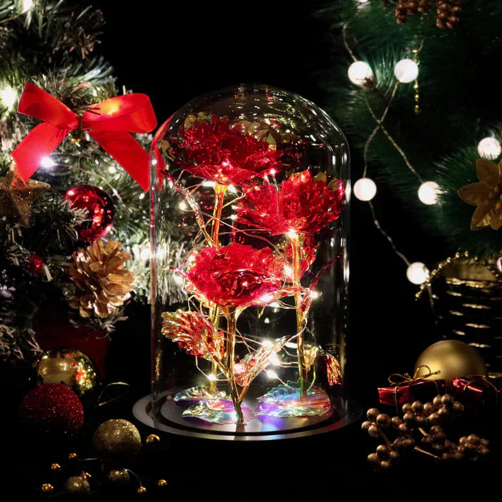 Enchanted LED rose in glass dome, iridescent red petals, gold-leaf stems, warm white LED lights, wooden base. Perfect gift.