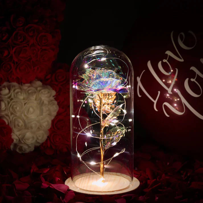Iridescent LED rose in glass dome with warm fairy lights, gold stem, wooden base; perfect gift.