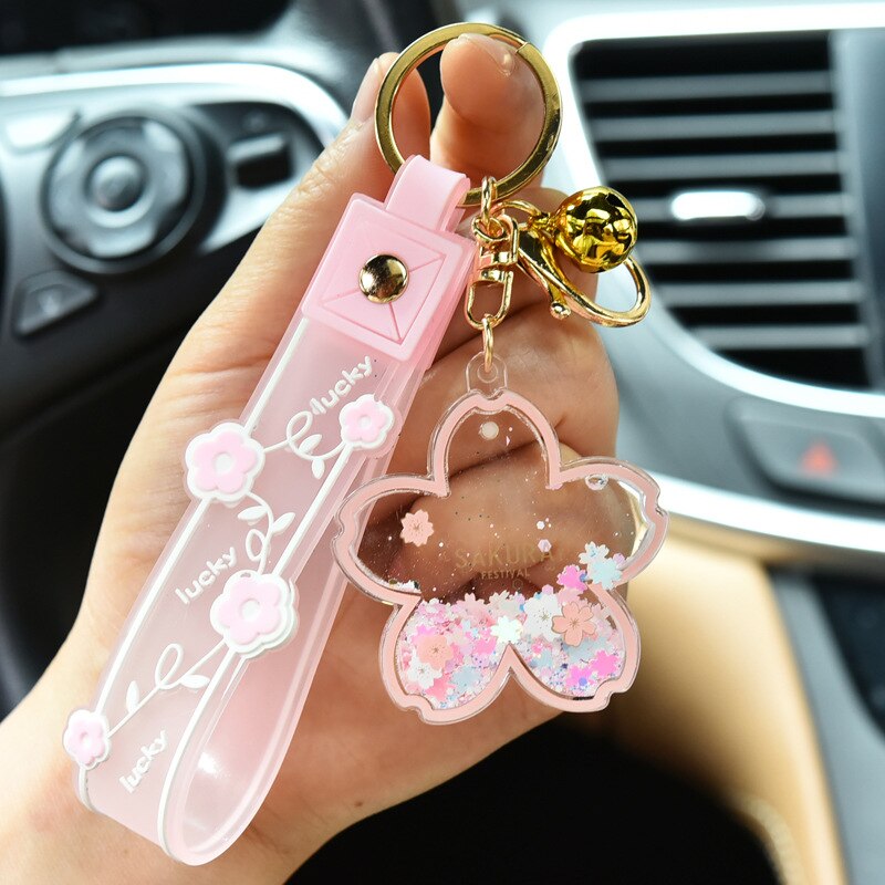 Pink sakura cow quicksand keychain with gold bell charm; resin and zinc alloy; features glitter swirl.