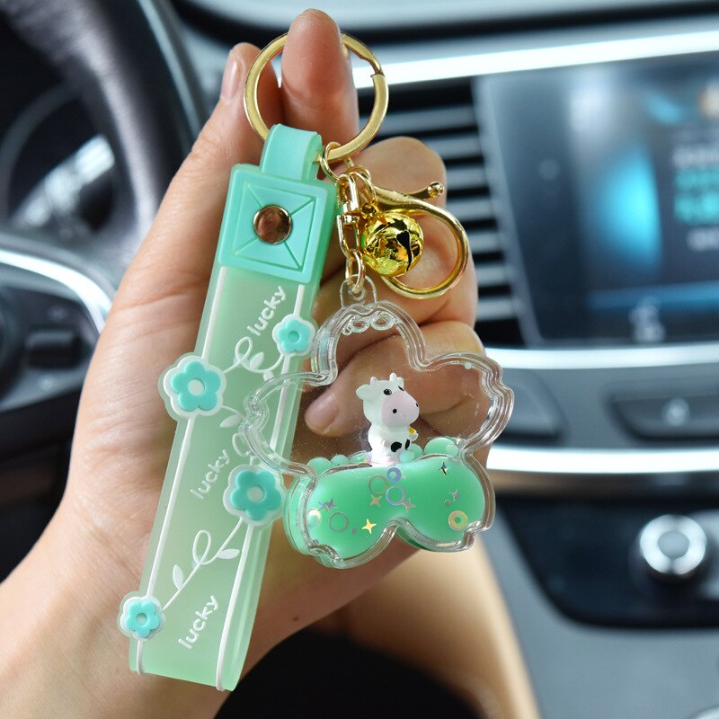 Cute green Sakura cow quicksand keychain with gold bell, featuring a charming cow figurine in a flower-shaped resin charm.