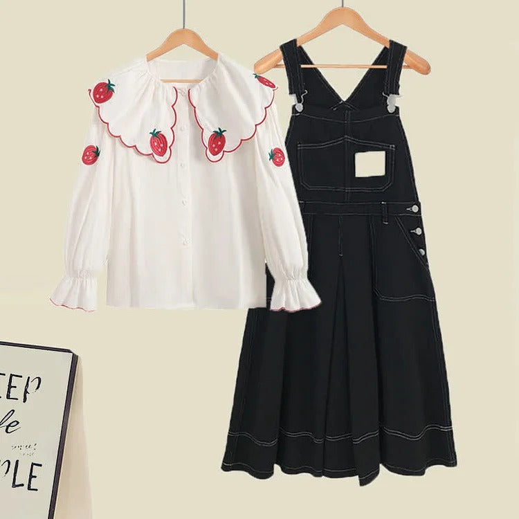 White long-sleeve shirt with strawberry embroidery and black denim overall dress; preppy style.