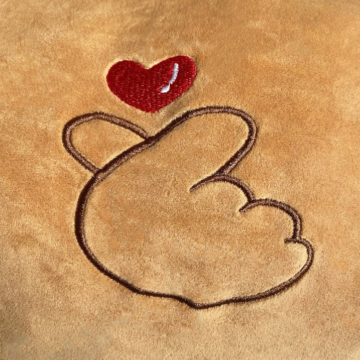 Tan Chum Chum plush body pillow with embroidered heart and hand gesture, filled with hypoallergenic PP cotton, zipper closure.