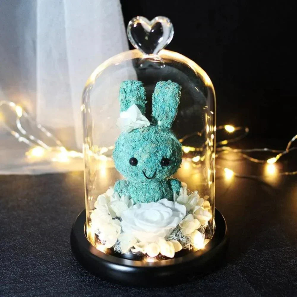 Teal bunny & preserved white rose LED display in glass dome; heart-shaped top, battery-operated, perfect gift.