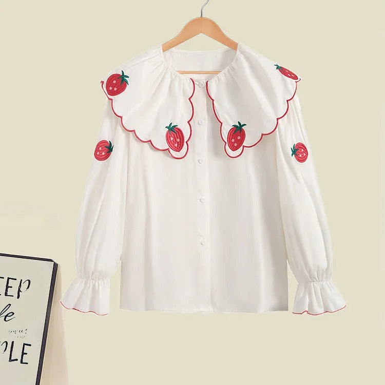 White long-sleeve blouse with strawberry embroidery, Peter Pan collar, and ruffled cuffs.  Polyester fabric.