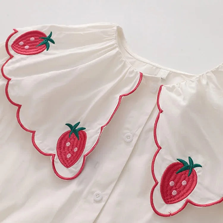 White polyester shirt with strawberry embroidery, peter pan collar, long sleeves. Part of a two-piece denim overall dress set.